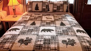 A bedroom with a large bed, a window with curtains, a lamp on a bedside table, and a wooden wall. - The Wilderness Inn (Wilmington)