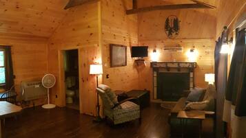 A cozy cabin interior with a wooden ceiling, a fireplace, a television, and a dining area.