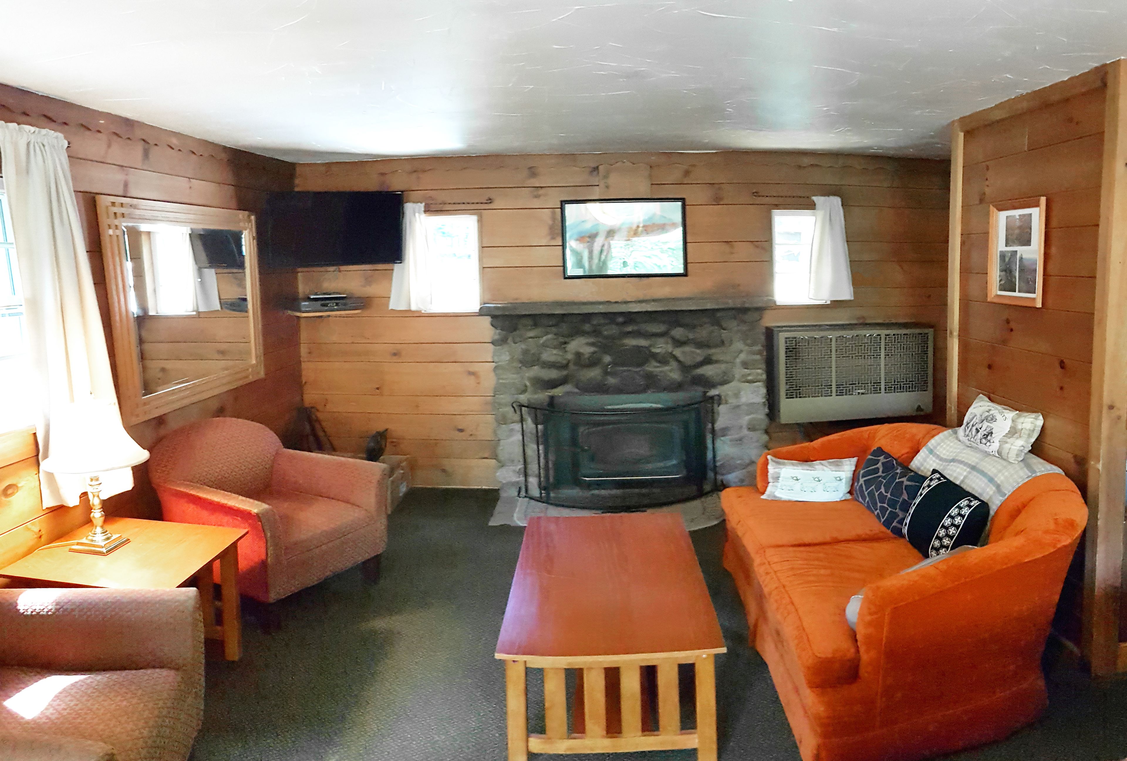 A cozy cabin interior with a stone fireplace, wooden walls, a sofa, a chair, and a small table.