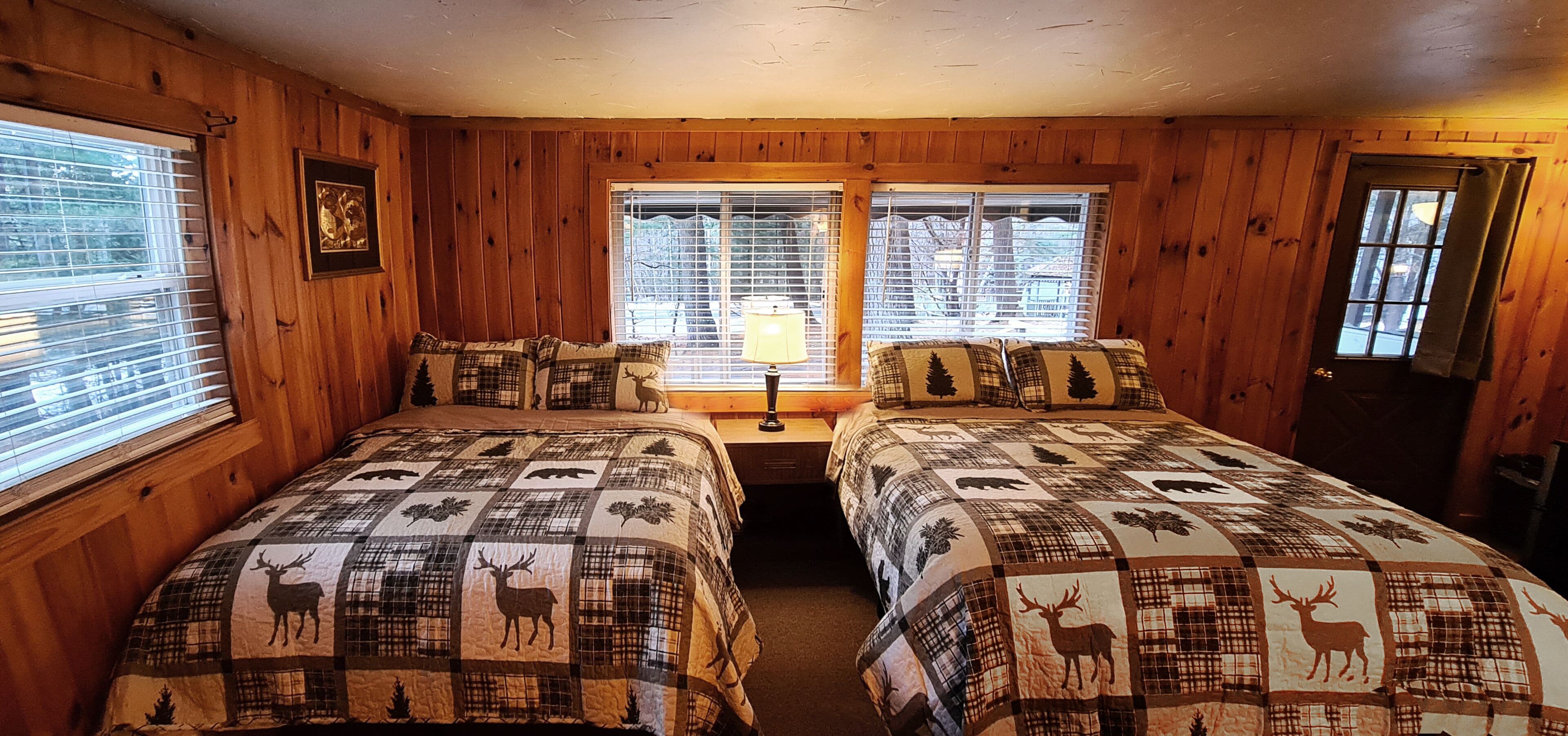 Una habitación tipo cabaña con dos camas, paredes de madera y ventanas amplias.