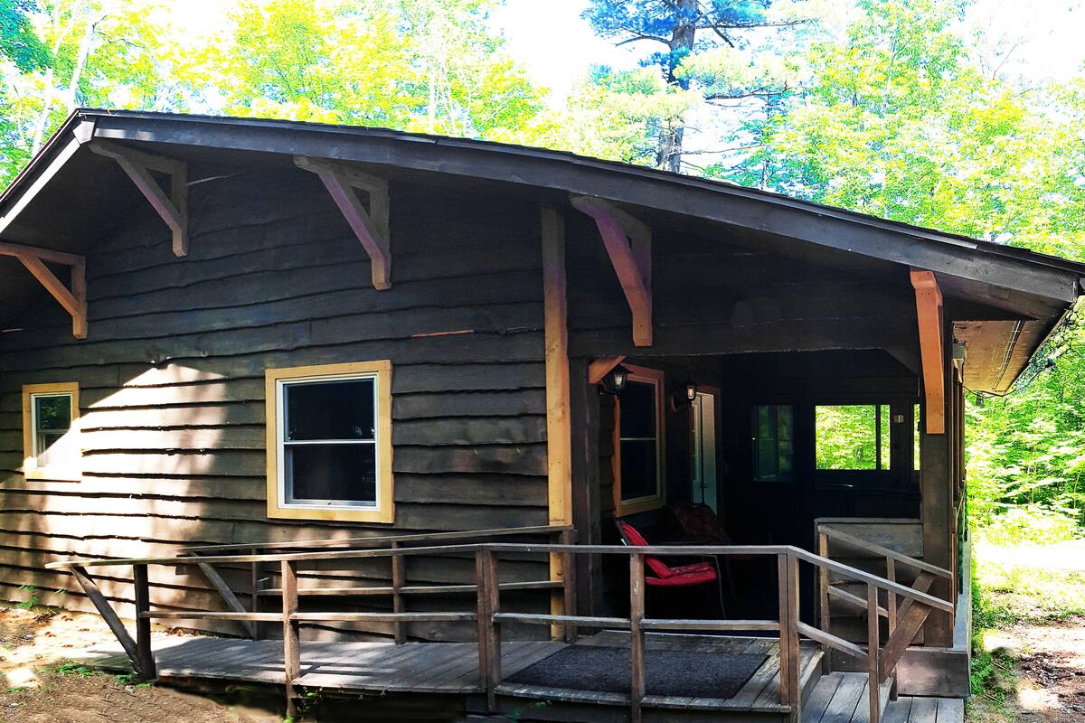 A rustic cabin with a porch, wooden railings, and a door leading to the interior.