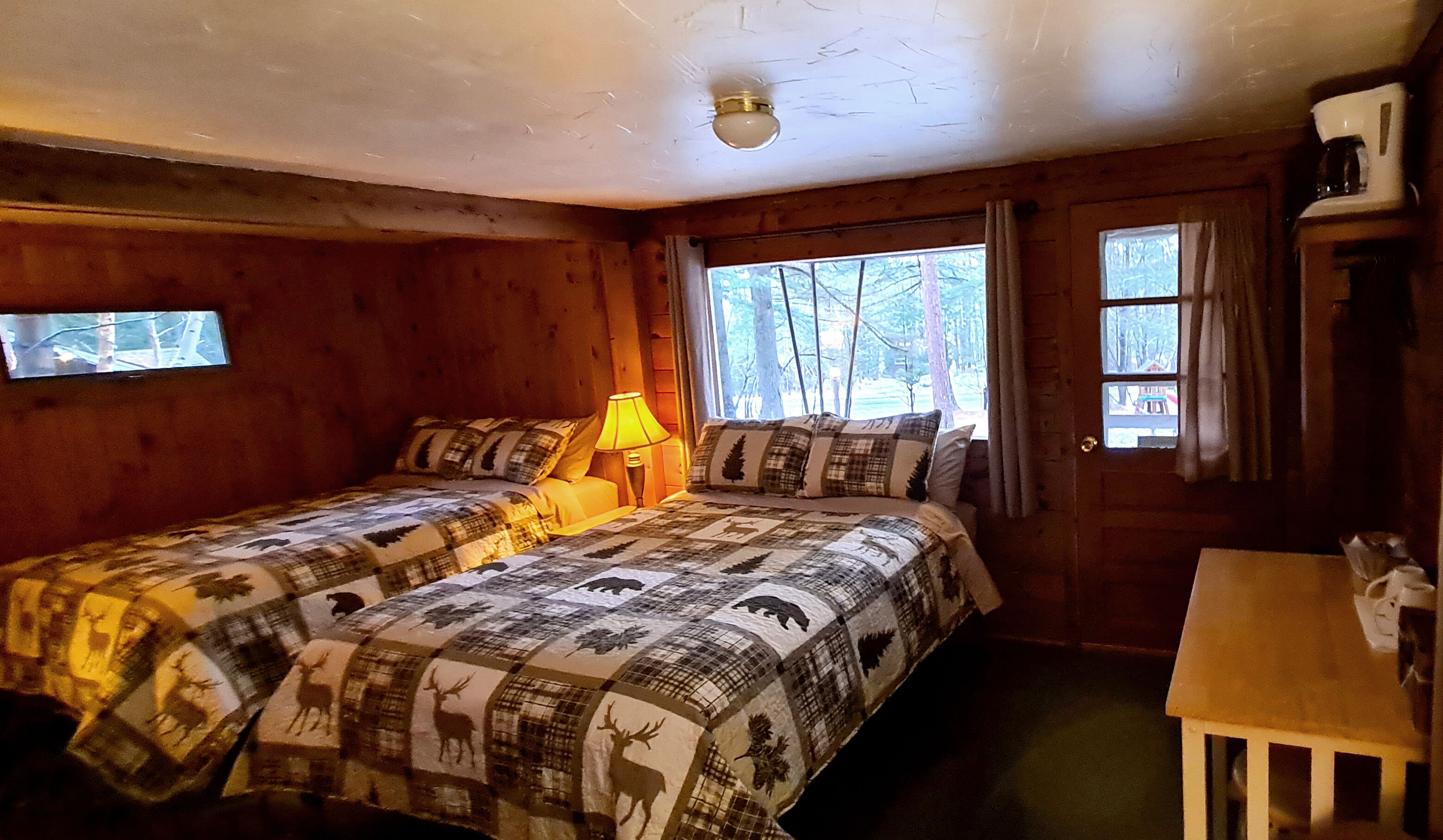 Une pièce confortable avec deux lits, une fenêtre donnant sur les arbres, une lampe et une petite table.