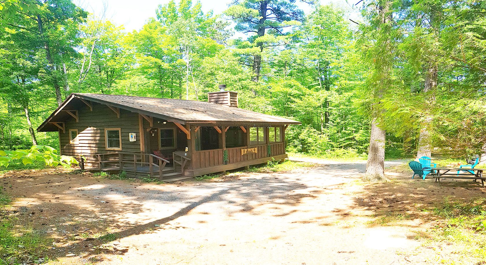 A rustic cabin with a porch, a picnic table, and chairs in a forest setting.