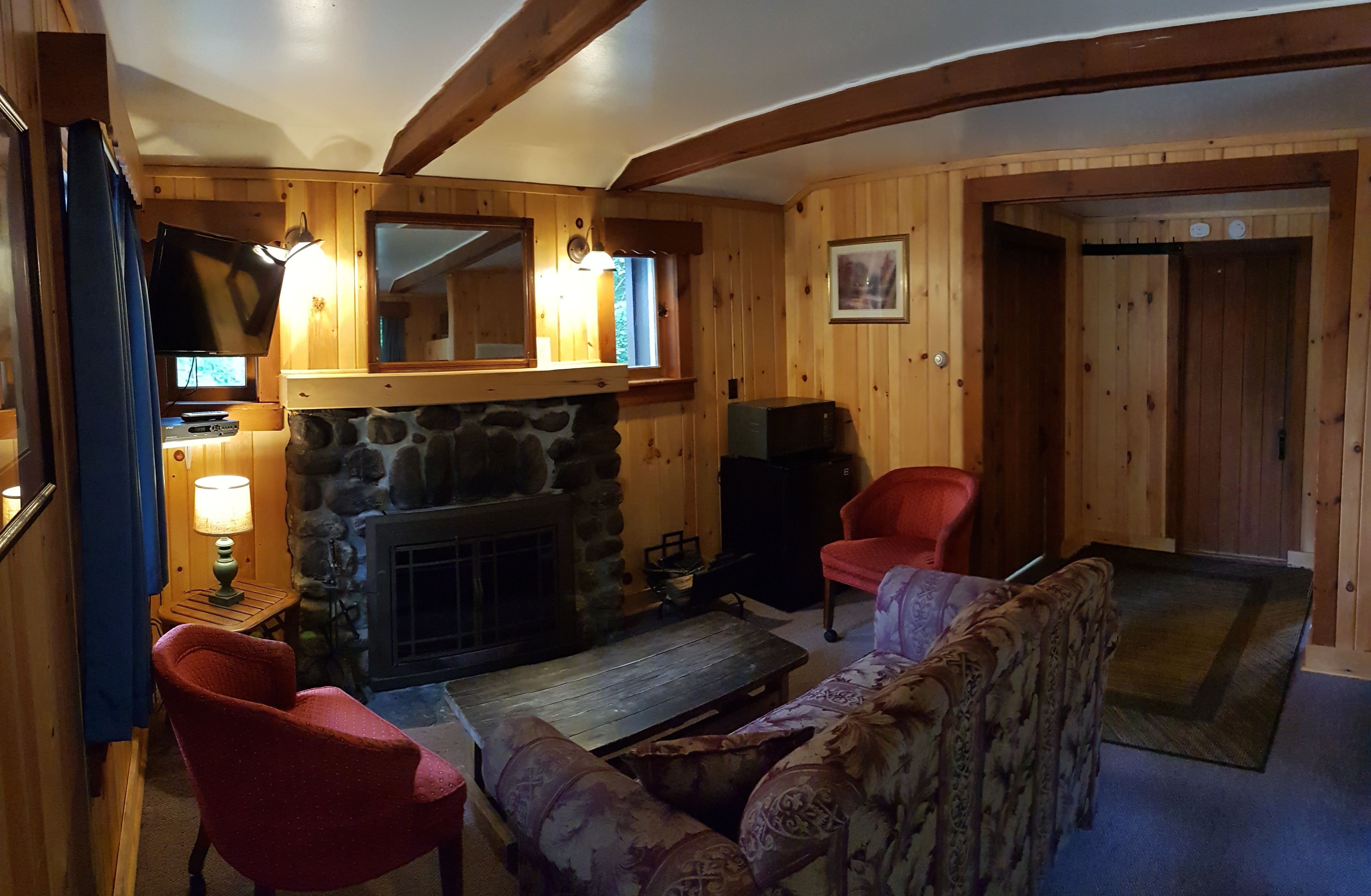 A cozy cabin interior with a stone fireplace, wooden walls, a television, and a red chair.
