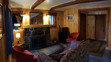 A cozy cabin interior with a stone fireplace, wooden walls, a television, and a red chair.