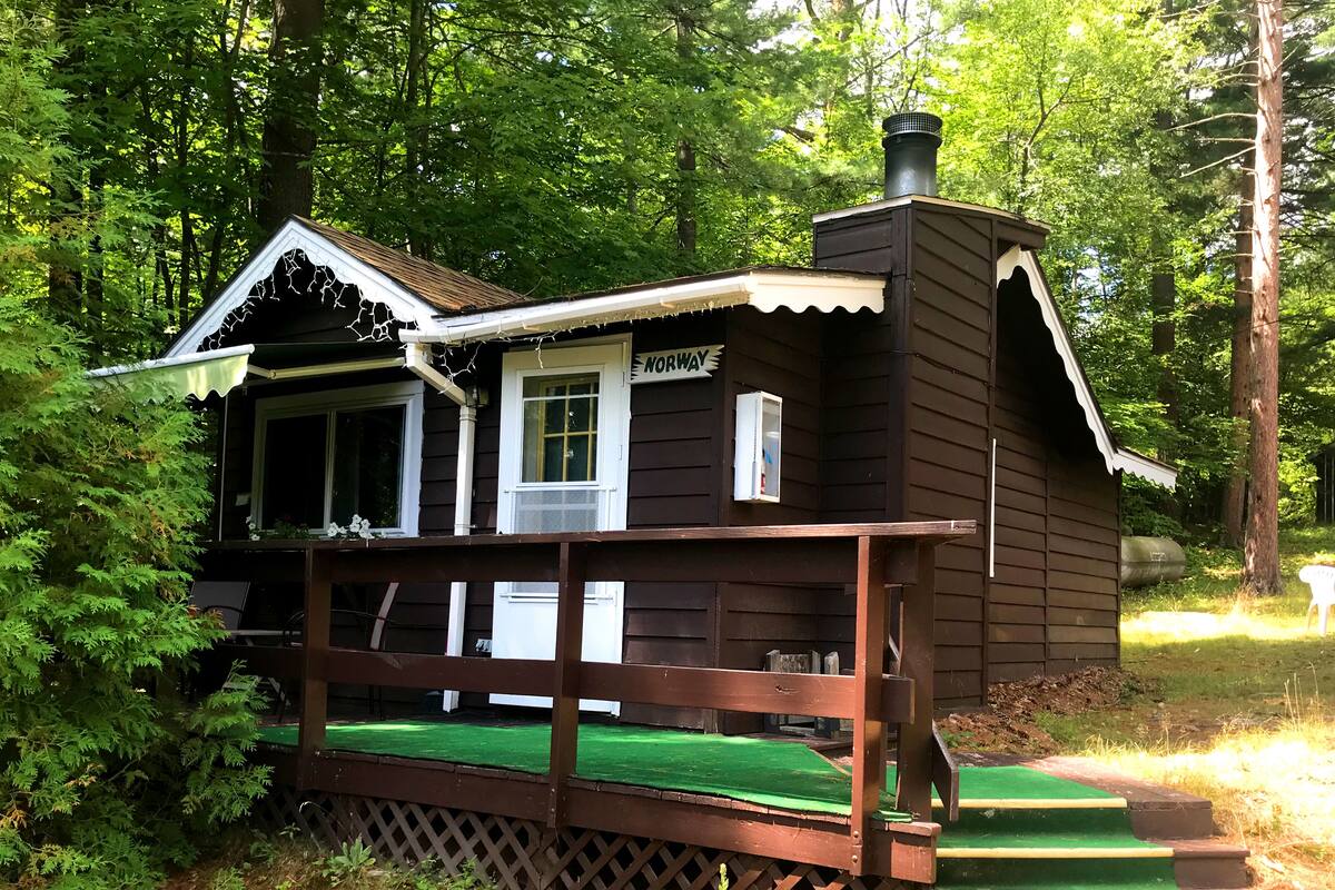A small cabin with a green deck, a chimney, and a window labeled "NORWAY".