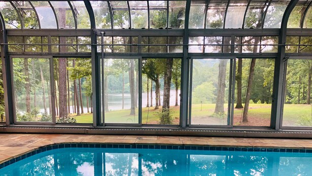 En swimmingpool med utsikt över en skog genom stora fönster.