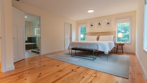 A spacious bedroom with a large bed, wooden flooring, and a view of the outdoors through a window.