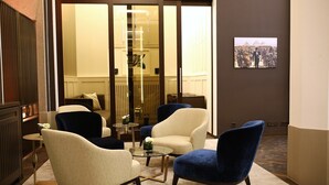 Un hall d’hôtel moderne, doté d’un espace détente avec des sièges, d’une cloison en verre et d’un tableau encadré au mur.