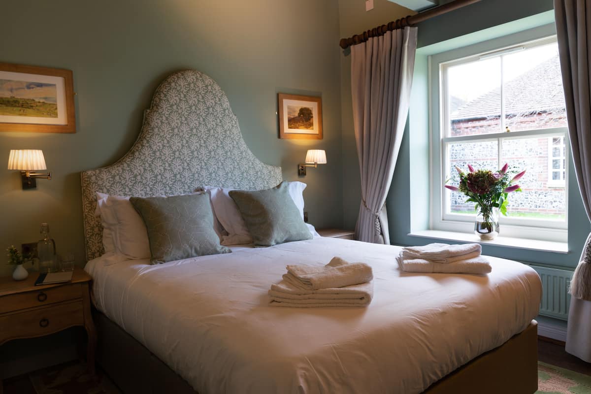 A neatly made bed with folded towels, a bedside lamp, and a framed picture on the nightstand.