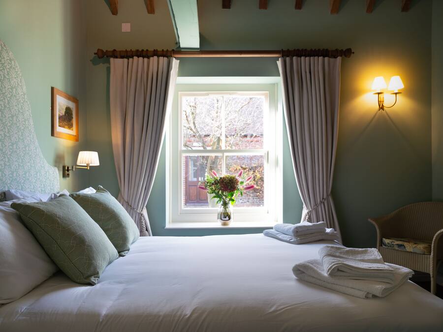 A neatly made bed with pillows, a vase with flowers, and a window with curtains.