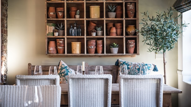 Een kamer met rieten meubilair, een houten plank met terracotta potten, en een plant in pot.