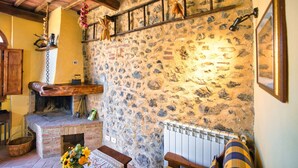 Una habitación rústica con pared de piedra, vigas de madera, chimenea y radiador.