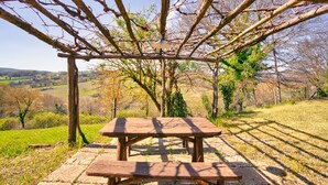 Una mesa de picnic de madera bajo una pérgola cubierta de hiedra en un paisaje rural.