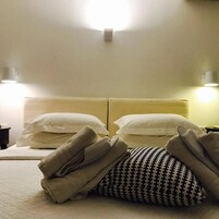 Quarto de hotel com cama de casal, duas luminárias de cabeceira e cabeceira com iluminação.