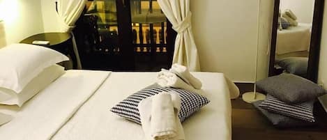 A hotel room with a bed, a chair, a table, a lamp, and a mirror.