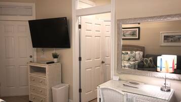 Una camera da letto con televisione a parete, un comodino con lampada, uno specchio e una porta che dà su un'altra stanza.