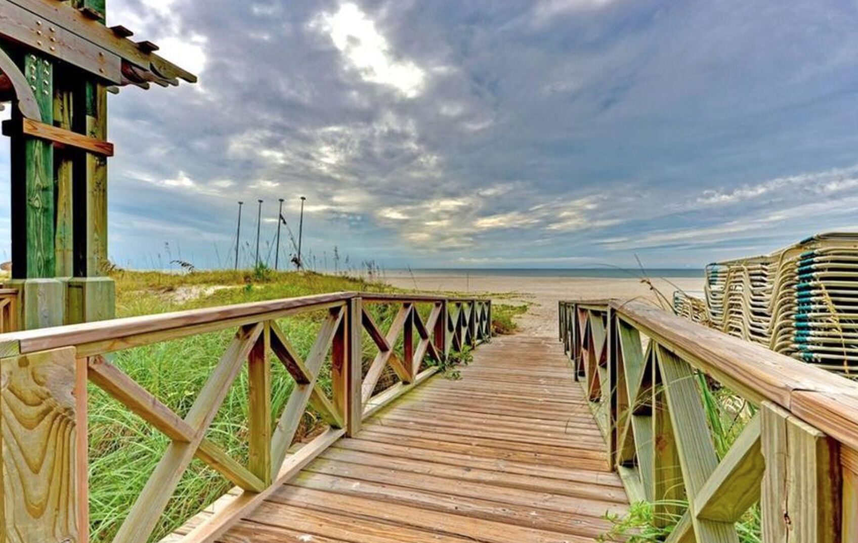 A wooden boardwalk leading to a beach with a cloudy sky.