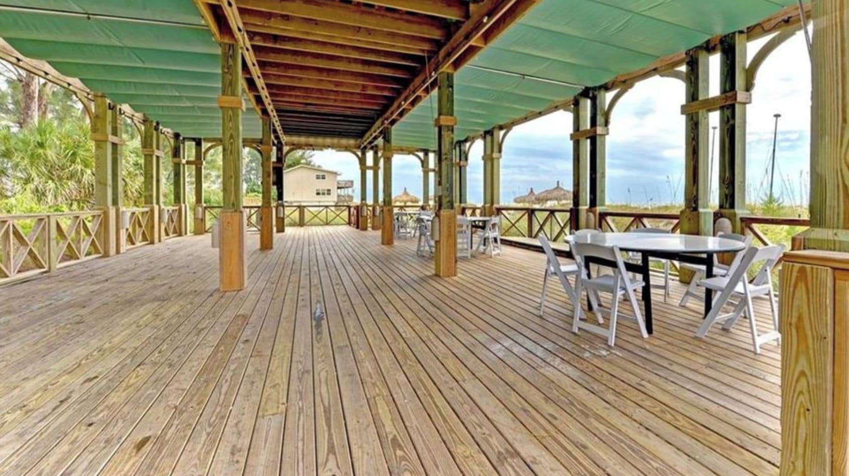 A covered wooden deck with tables and chairs, overlooking a beach.