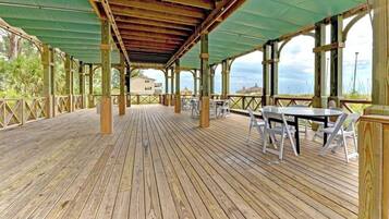 A covered wooden deck with tables and chairs, overlooking a beach.