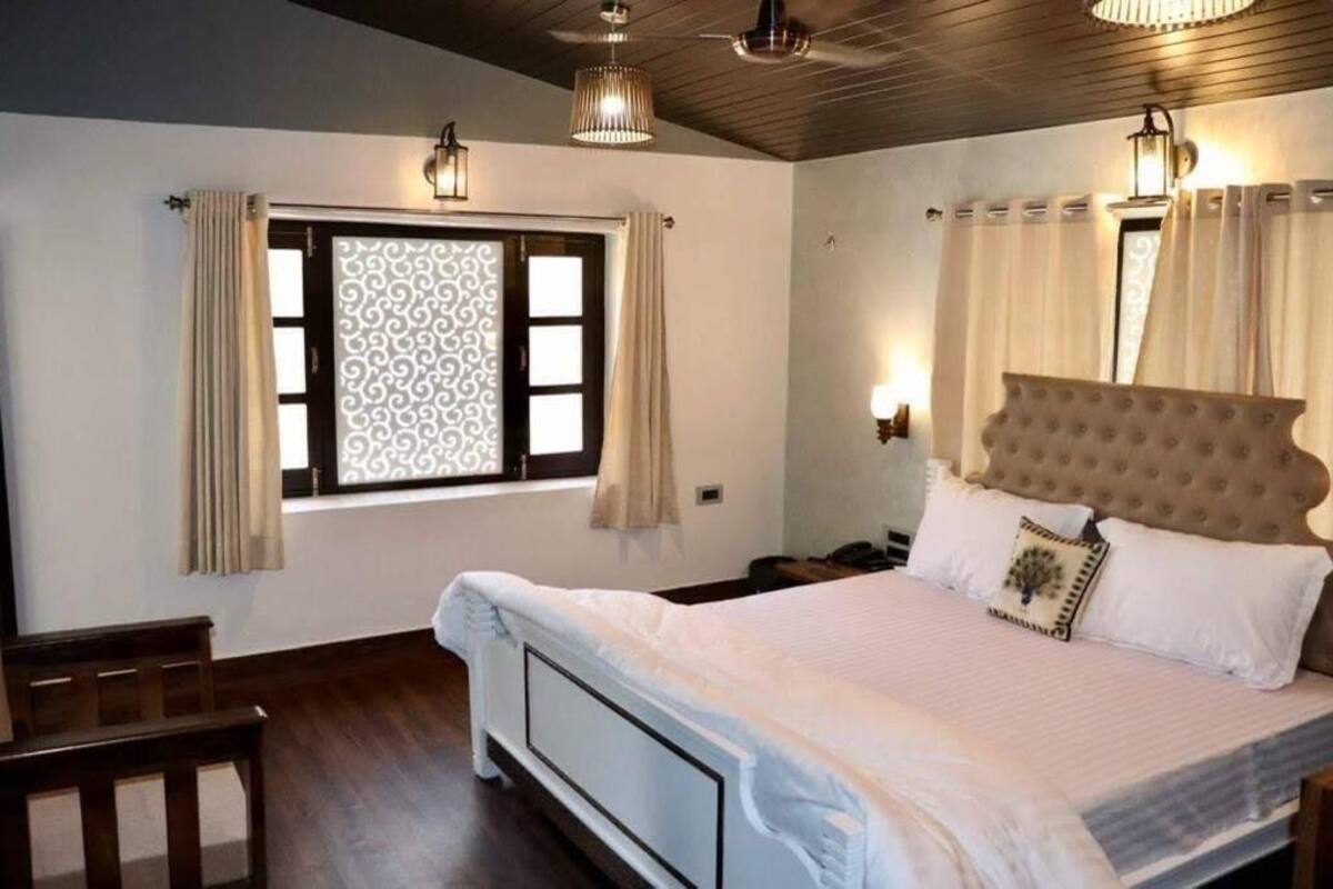 A bedroom with a bed, a window with curtains, a bedside table, and a lamp.