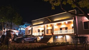 A two-story building with a porch, steps leading to the entrance, and a car parked in front.
