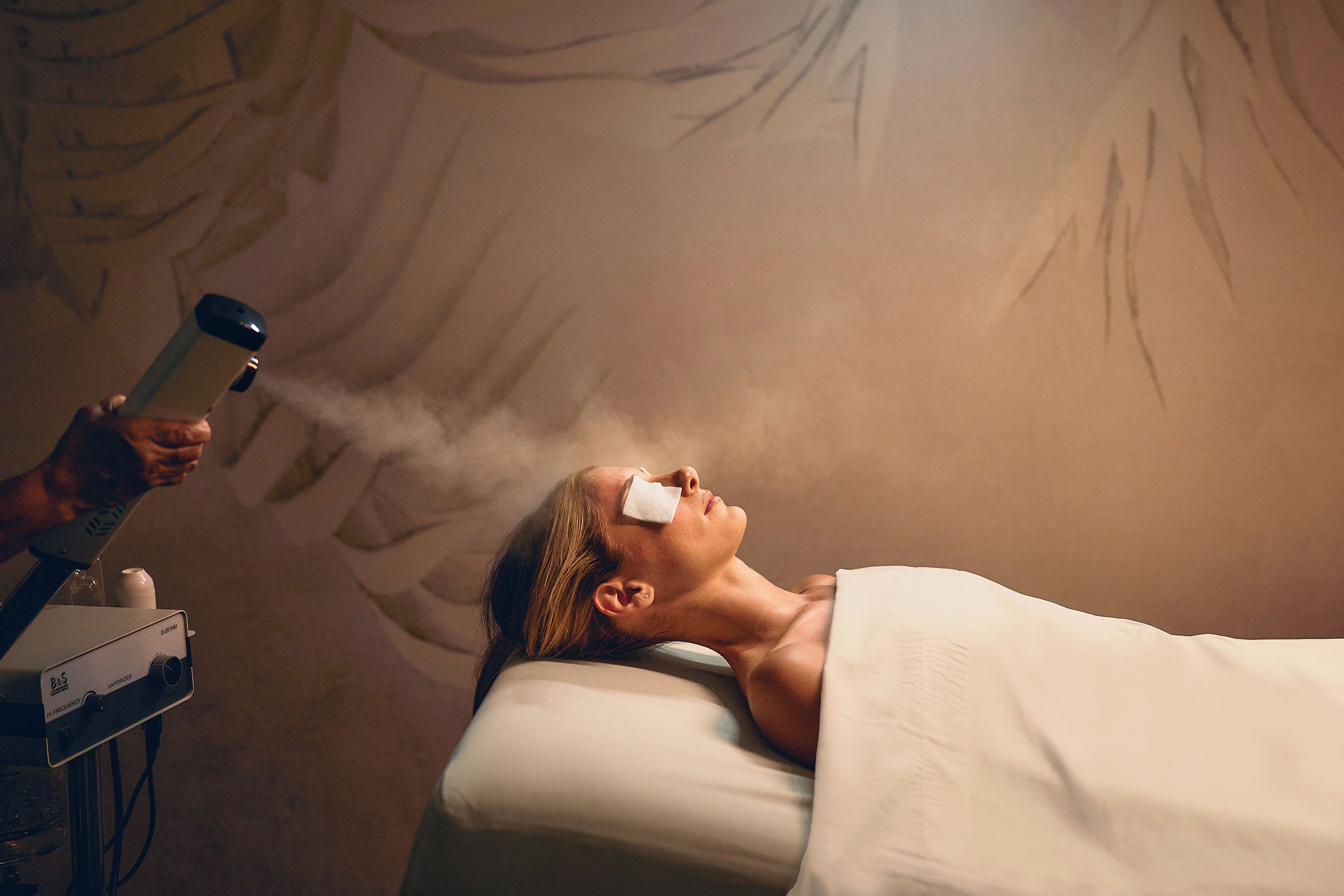 Una persona acostada con un vaporizador que emite vapor hacia su rostro.
