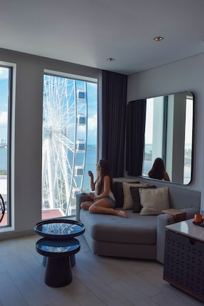 A modern living room with a large window, a sofa, a coffee table, and a mirror reflecting the room. - Canopy by Hilton Cancun La Isla (Cancun)