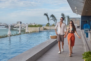 A couple walking by a pool with a city view, a covered area, and outdoor seating. - Canopy by Hilton Cancun La Isla (Cancun)