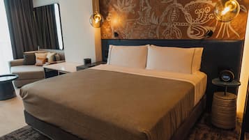 A modern hotel room with a large bed, a sofa, a small table, and a wall-mounted clock.