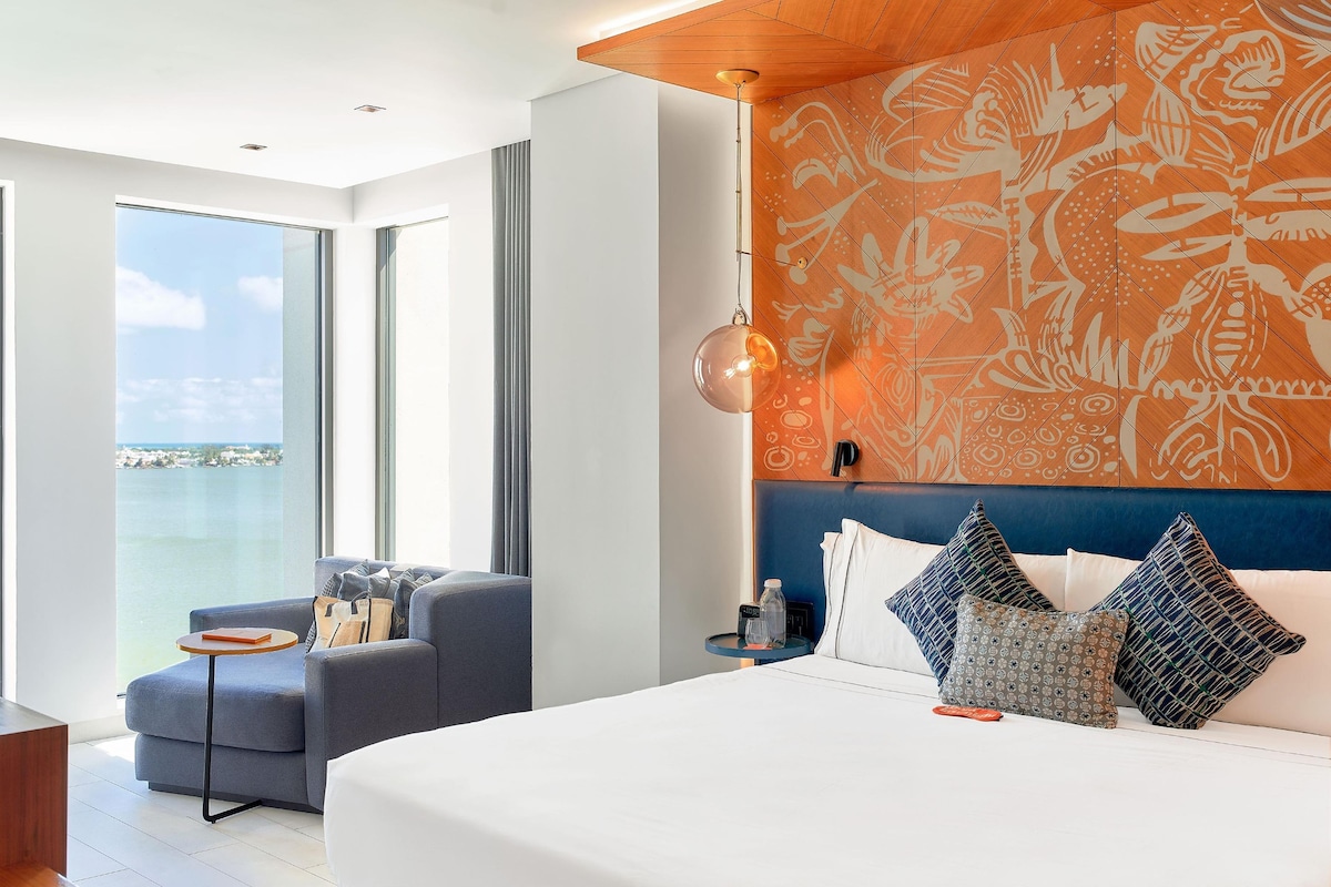 A modern hotel room with a large bed, a seating area with a view, and a patterned wall.
