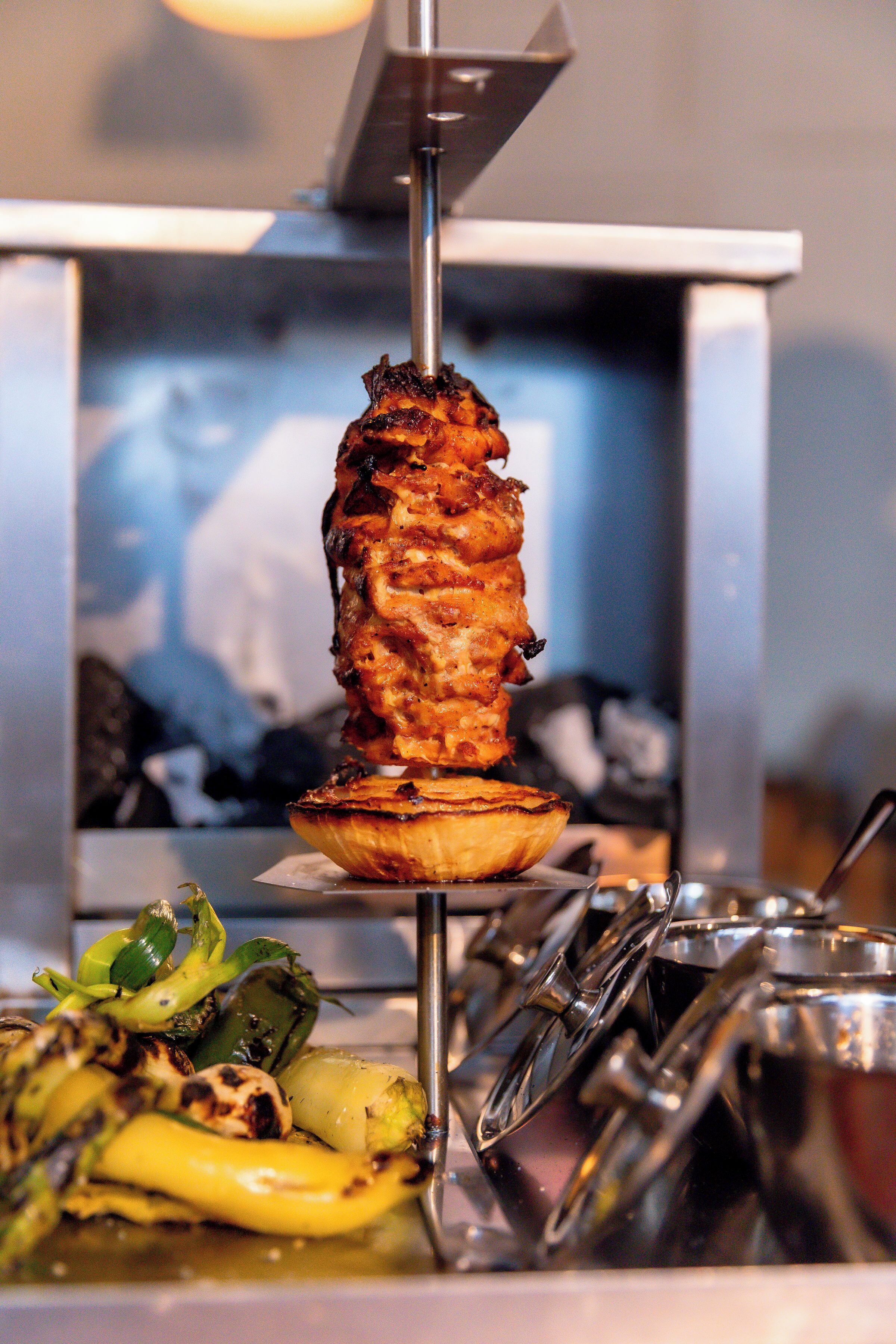 Um espeto giratório vertical com carne grelhada e legumes.