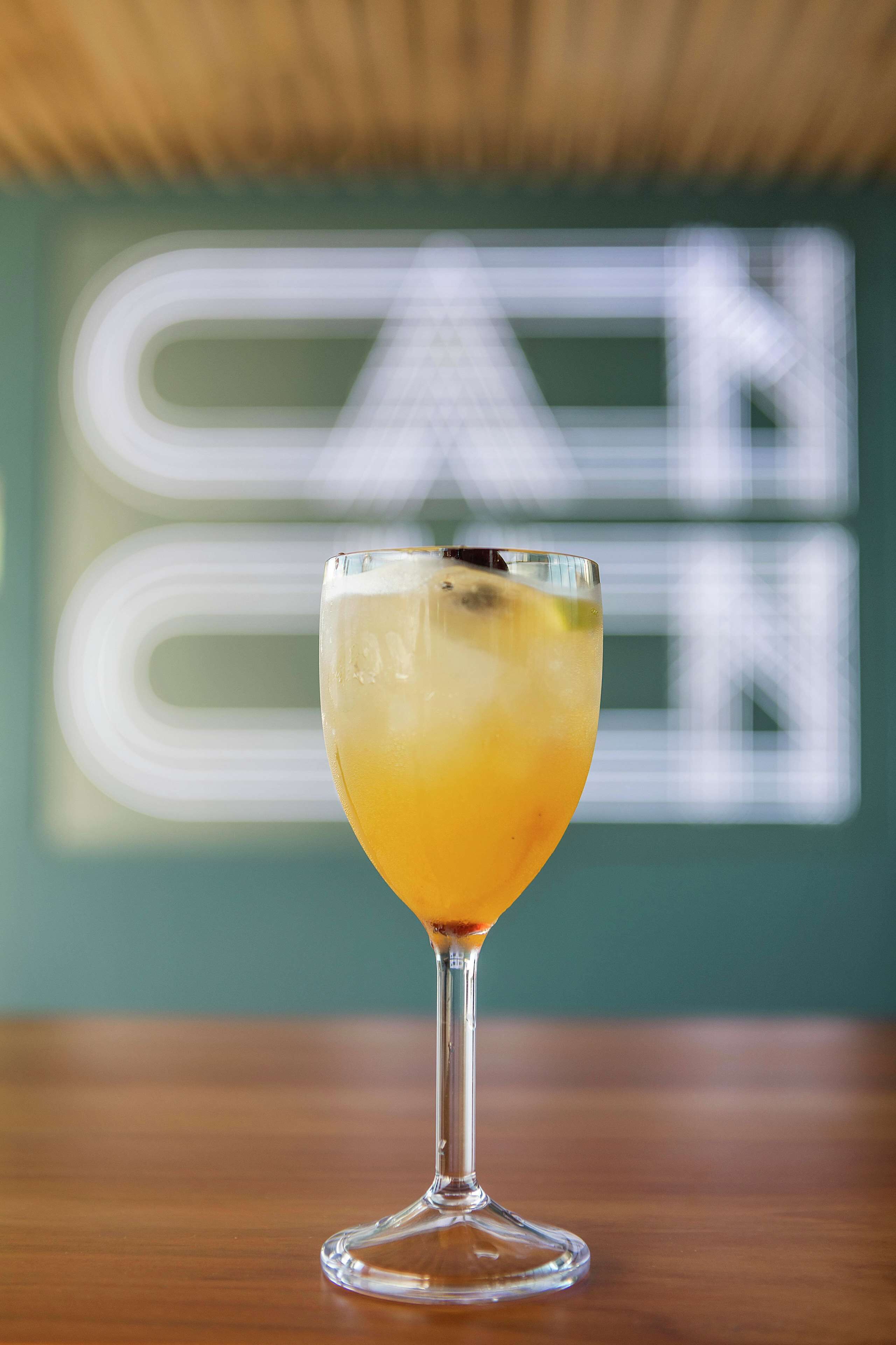 A cocktail glass on a wooden surface with a blurred background featuring a large, stylized letter 'N'.