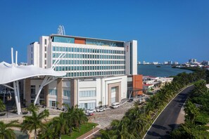 A modern hotel with a glass facade, a parking area, and a view of the sea.