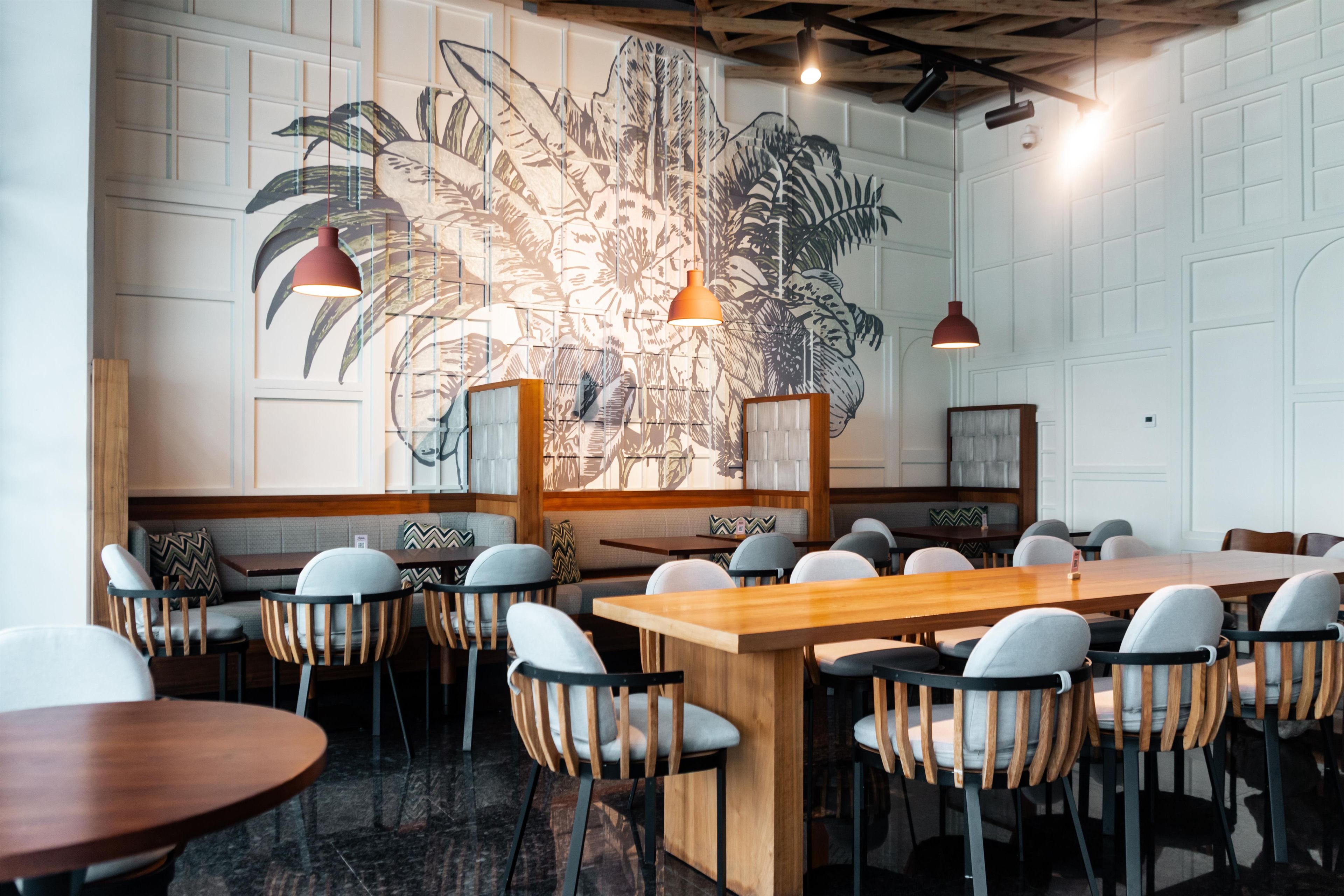 Interior de restaurante com uma mesa de madeira comprida, várias cadeiras e um grande mural na parede.
