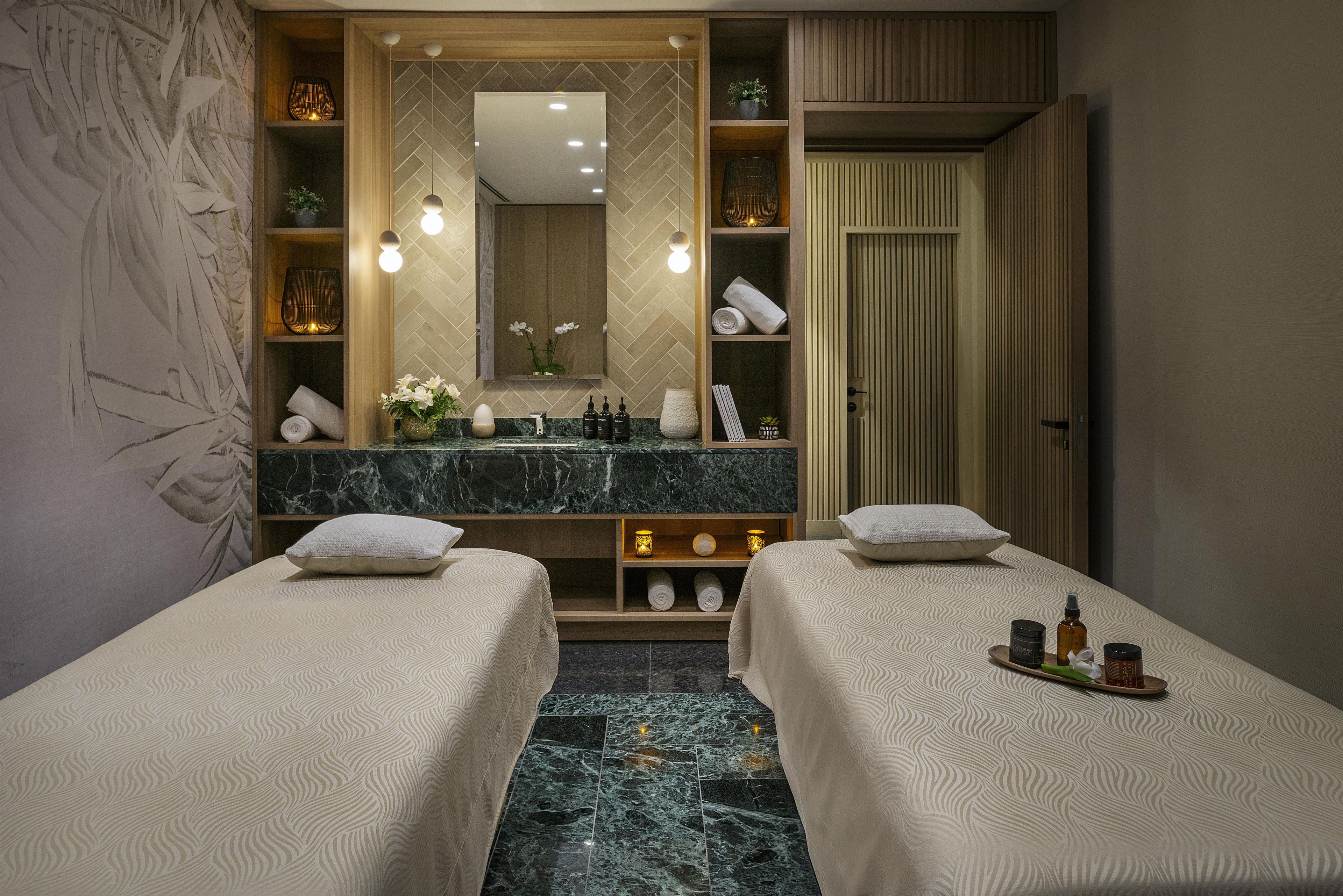 Habitación de hotel con dos camas, un espejo grande, una tocador con artículos de aseo y suelo de mármol.