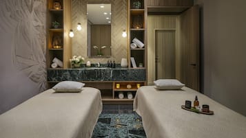Habitación de hotel con dos camas, un espejo grande, una tocador con artículos de aseo y suelo de mármol.