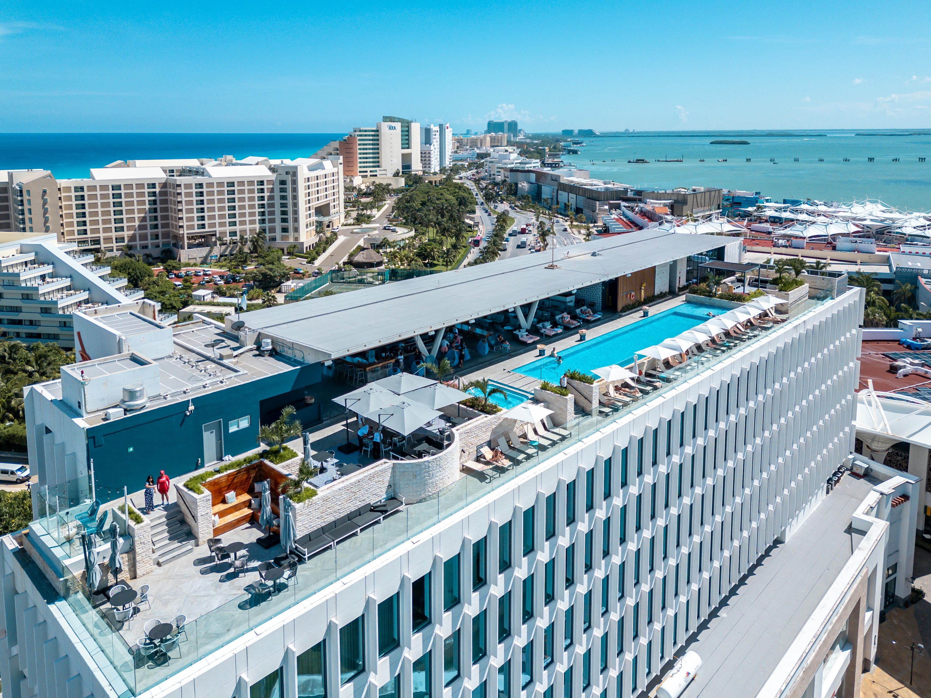 Un hotel moderno con piscina en la azotea, con vistas al océano y al paisaje urbano.