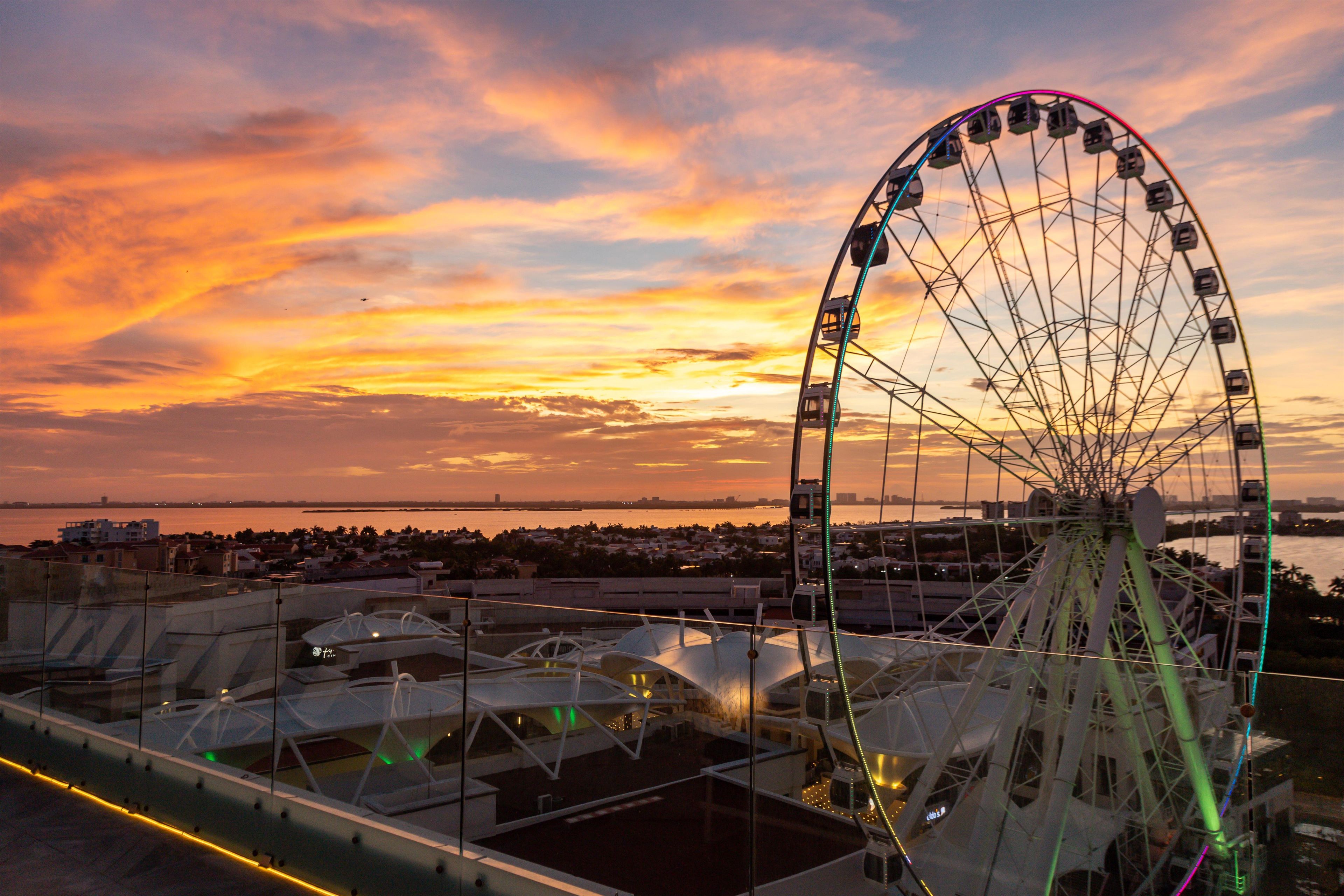 Una noria al atardecer con vistas al paseo marítimo y edificios de fondo.