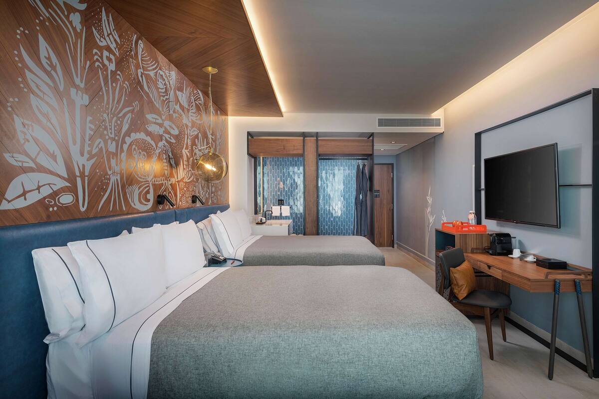 Una habitación de hotel moderna con dos camas, un escritorio, un televisor y una decoración mural.