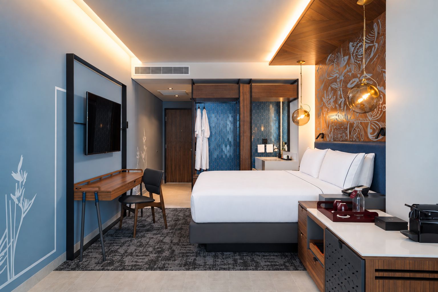 A modern hotel room with a bed, desk, chair, and a TV.