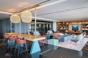 A modern lounge area with a long wooden table, multiple seating options including sofas and chairs, and a patterned rug.