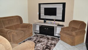 A living room with two brown sofas, a flat-screen TV on a stand, and a small table with a remote control and decorative items. - HOUSE WITH HEATED POOL Solar, air conditioning, Wi-Fi, and TV with Netflix! Sleeps 13 people (Olímpia)
