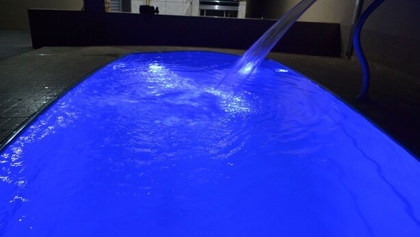A blue-lit pool with a water fountain. - HOUSE WITH HEATED POOL Solar, air conditioning, Wi-Fi, and TV with Netflix! Sleeps 13 people (Olímpia)