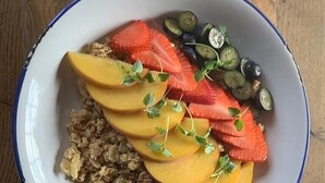 Eine Schüssel Haferflocken, belegt mit geschnittenen Erdbeeren, Blaubeeren und Pfirsichen, garniert mit Petersilie.