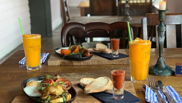 Ein Esstisch mit einer Mahlzeit aus Eiern, Gemüse und Brot, begleitet von zwei Gläsern Orangensaft und einer Kerze.