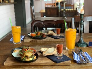 A dining table with a meal consisting of eggs, vegetables, and bread, accompanied by two glasses of orange juice and a candle. - Chequers Inn (Battle)