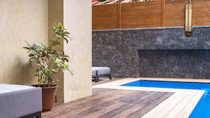 Un espace piscine doté d’une terrasse en bois, d’un mur en pierre et d’une plante en pot.