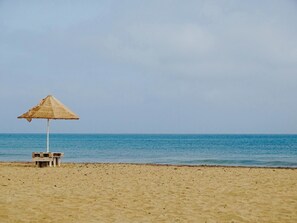A beach with a thatched umbrella and a small wooden structure. - Angulo House (Sal)