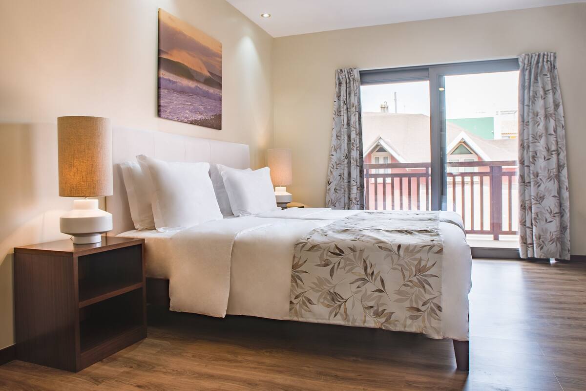 Une chambre à coucher avec un lit, des tables de chevet, un tableau et une vue par la fenêtre.